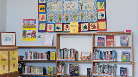 Image of inside library with bookshelves and quilt hanging on the wall.